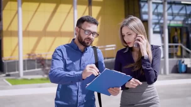 Gerentes durante el almuerzo en el patio de un edificio de oficinas. La chica está hablando por teléfono y al mismo tiempo ayuda al entrenador en prácticas . — Vídeos de Stock