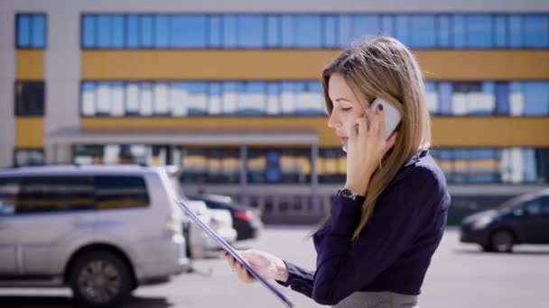 Prédios de escritórios. A menina vai trabalhar calmamente e fala ao telefone sobre questões de trabalho. O gerente falando . — Vídeo de Stock