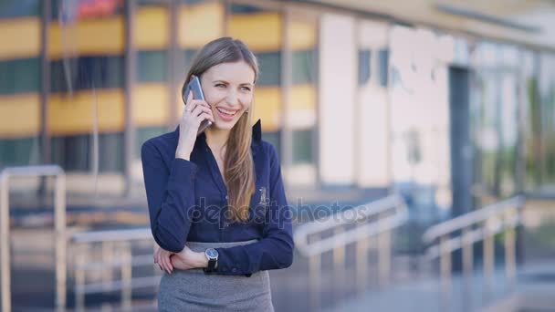Γυναίκα των επιχειρήσεων στη αυλή του ένα επιχειρηματικό κέντρο. Μια γυναίκα είναι να μιλάμε στο τηλέφωνο κατά τη διάρκεια ενός διαλείμματος. Ένα νεαρό κορίτσι σε καλή διάθεση. — Αρχείο Βίντεο