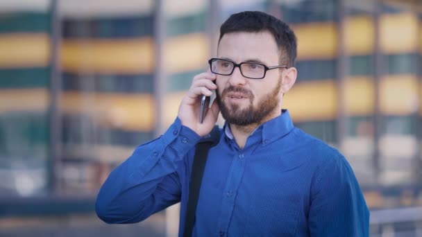 Üzletember, az udvarban, a business centerben. Egy ember beszél telefonon, közben egy kis szünetet. Egy fiatal férfi is nagyon koncentrált. — Stock videók