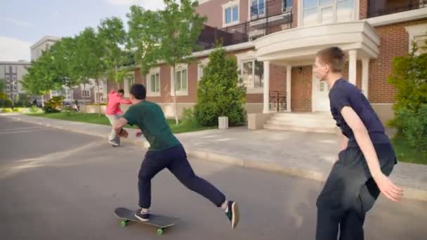 Vários homens jovens vão em skates em um estilo livre no asfalto durante o dia, os caras rolam rapidamente nas tábuas, empurrando seus pés para fora da estrada — Vídeo de Stock