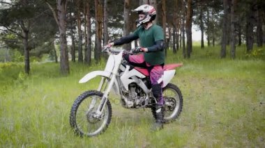 Yetişkin bir adam koruyucu bir kask ve eklemleri kendi ayakları üzerinde sürme için ormanlık duruyor bir dağ bisikleti rüzgarlar