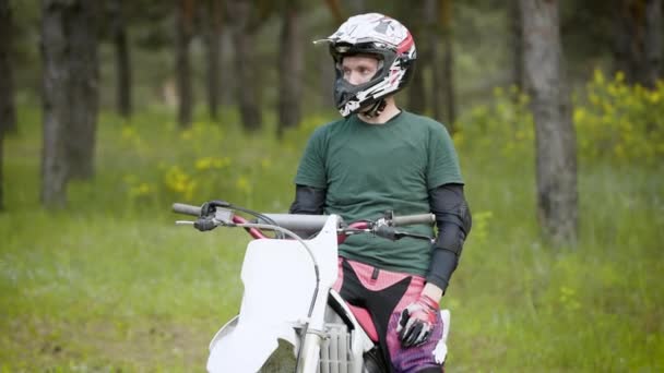 Um jovem que se senta em uma motocicleta descansa na floresta, as pessoas no capacete gostam da música na natureza. — Vídeo de Stock