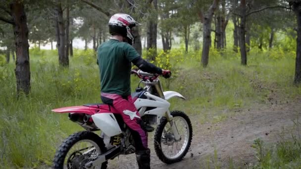 En idrottsman som bär en skyddande hjälm och speciella uniform rider en cross-country motorcykel på en skog del i naturen — Stockvideo