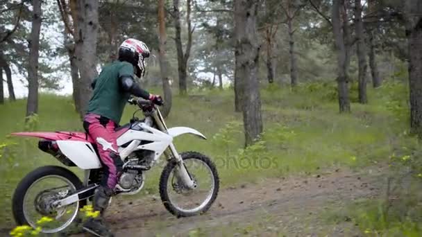 Un atleta in uniforme protettiva e un casco in testa cavalca su una moto sportiva universale nella parte forestale superando le difficoltà — Video Stock