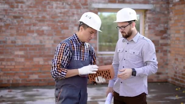 Unga manliga builder visar tegel till hans förman — Stockvideo