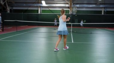 Genç bir atlet onun ortakları ile eğitim sırasında tenis topları beats, spor kıyafetli bir kadın aktif olarak Tenis Kortu çalışır