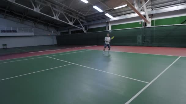 Een volwassen man speelt tennis, een atleet slaat de bal via het net met een racket, speelt hij met een partner op de baan — Stockvideo