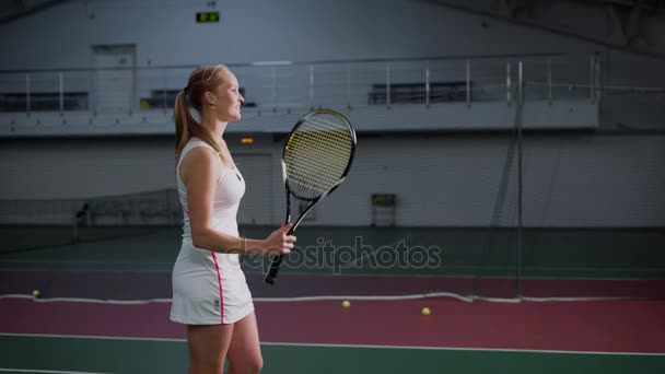 Молодая женщина со светлыми волосами крутит и бросает теннисную ракетку на руки, спортсмен с улыбкой стоит на теннисном корте, где проходят спортивные соревнования — стоковое видео
