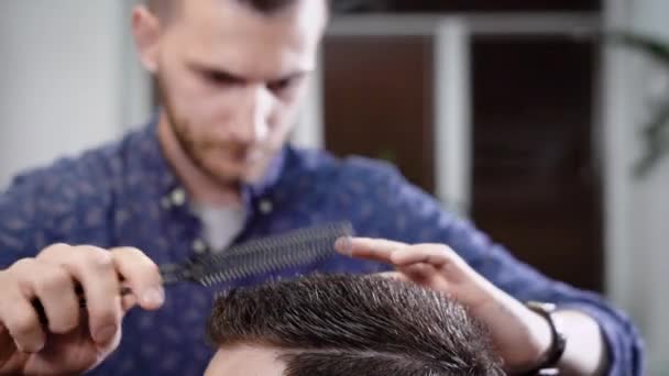 Close up shot of the head of a man who combs his hair and makes a fashionable styling in barbershop with a comb and a hair gel — Stock Video