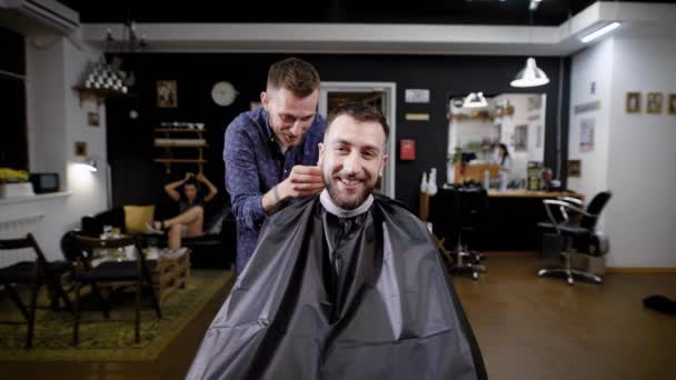 Un peluquero elegante habla con un visitante de salón de belleza que vino a conseguir uqdaku y refrescar un corte de pelo en la barbería, el visitante es feliz — Vídeos de Stock