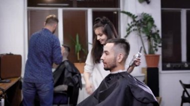 Şık ve genç kadın Kuaför Saç düzeltici eline alır ve saç şekillendirme ve bir güzellik salonu için saç kesimi için bir adam yapmak başlar