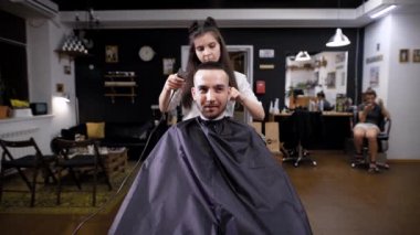 Güzel bir kadın, bir saç stilisti saçını trimmra ile uzunluğu için saçlarını kısaltır, görüntünün tamamlanması bir koltukta oturan bir adam bekliyor
