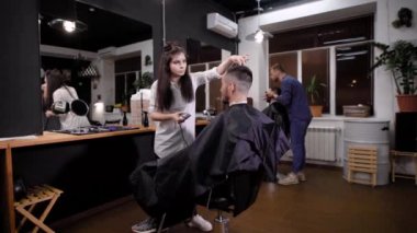 Güzellik Salonu istemcileri bir genç kadın stilist tarafından kesilmiş saç patlama ile bir düzeltici ziyaretçi berber dükkanı için beklediği yeni bir saç modeli almak için