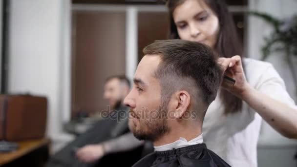 Una mujer adulta y elegante que es una joven y practicante estilista hace una nueva inmigración para un salón de belleza, un hombre con barba espera un corte de pelo — Vídeo de stock