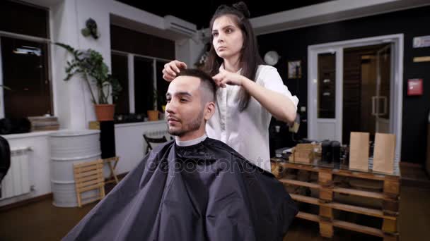 Uma mulher cabeleireira completa o estilo de cabelo para um visitante de uma barbearia, um cabeleireiro usa um gel para modelar o penteado — Vídeo de Stock