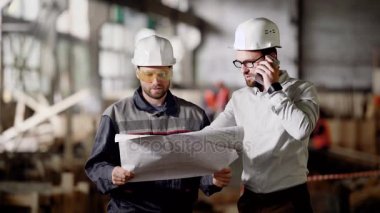 Bina inşaat işçileri. İnşaat işçisi ile proje planı Çekme Makinası tartışırken telefonu konuşurken denetçisi.