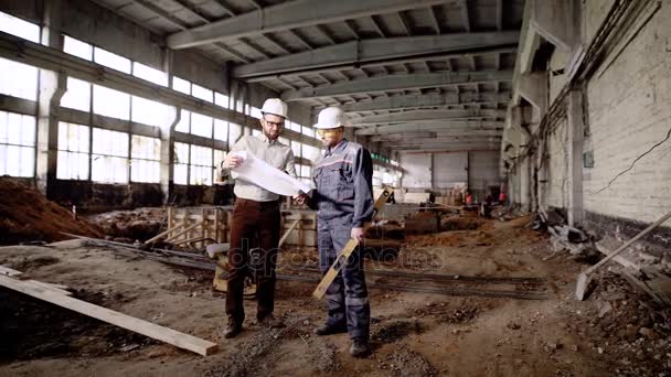 Danışman ve proje tartışıyor Yöneticisi. İki adam yıkılan bina ve proje planını tartışıyor içinde ayakta zor şapka. — Stok video