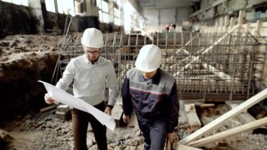 İki adam planı ile çalışma. Yüklenici ve blueprint soruşturma ve site arka plan üzerinde takım içinde çalışma işçisi.