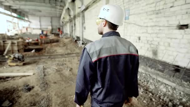 Vista trasera del trabajador de la construcción. Hombre anónimo en sombrero duro y uniforme caminando sobre el fondo del edificio destruido en el sitio . — Vídeos de Stock