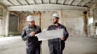 İnşaat İşçileri blueprint Çekme Makinası ile. Planı ile sitenin arka planda çalışan ve yeni plan tartışmaya iki adam.