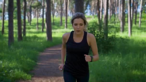 Молодая женщина в спортсменке бежит по дороге в летний лес — стоковое видео