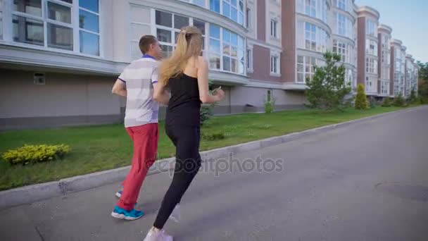 Two people running together alongside buildings on street in summer — Stock Video