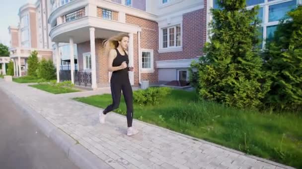 Deportiva corriendo a la luz del sol por la acera de la calle en verano — Vídeo de stock