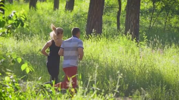 Двоє людей у спортивному одязі біжать на фоні зеленого дерева — стокове відео