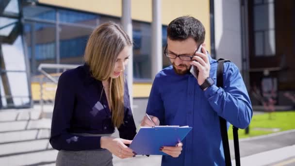 Biznesmen rozmowy telefon i podpisywania dokumentów. Zajęty Menedżer stoi w biurze budynku z partnerem i mówić jego smartphone podczas podpisywania dokumentów. — Wideo stockowe