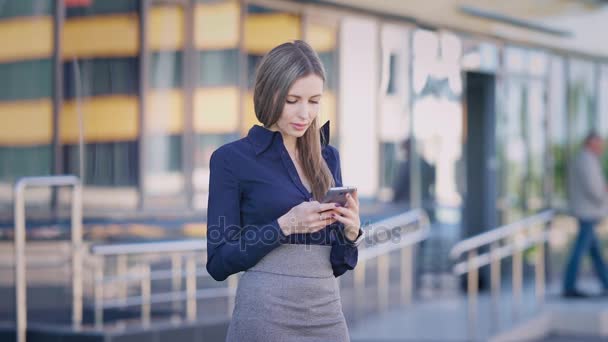 Donna d'affari che usa il telefono nell'edificio degli uffici. Giovane abbastanza fiducioso lavoratore donna ufficio in piedi e la navigazione smartphonein strada a edificio per uffici . — Video Stock