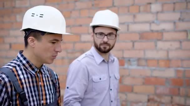 Builder promenader och kommunicera på bakgrund av tegelvägg — Stockvideo