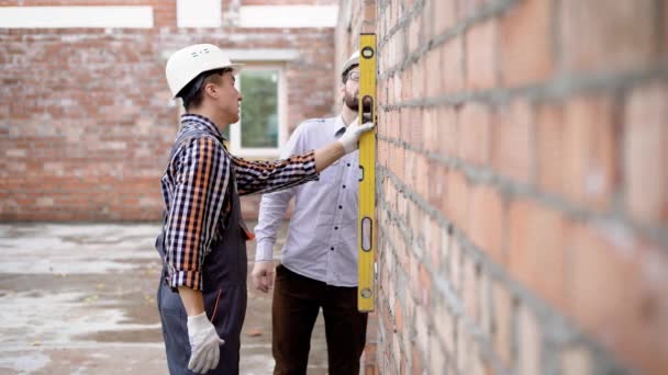 Two men in uniform measuring wall with instrument on site — Stock Video