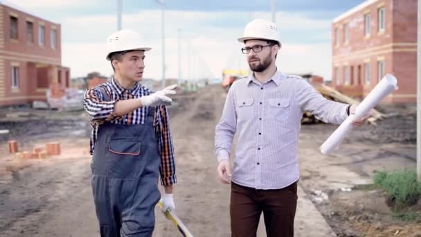 Dos hombres cotrabajando en un nuevo proyecto de construcción mientras caminan en el sitio — Vídeo de stock