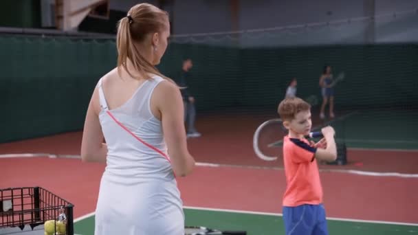 Instructora de tenis enseñando a un niño a golpear la pelota con una raqueta — Vídeo de stock