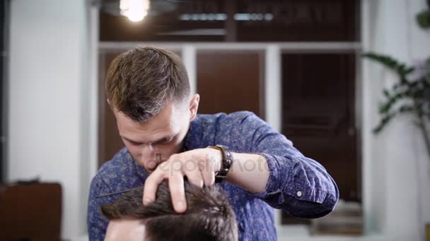 Człowiek stoi w salonie i przycinanie włosów na klienta, siedząc w fotelu — Wideo stockowe