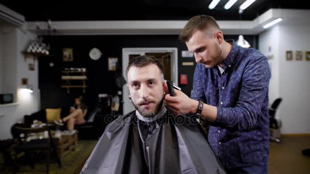 Peluquería profesional haciendo corte de pelo a cliente masculino elegante sentado en la barbería — Vídeos de Stock