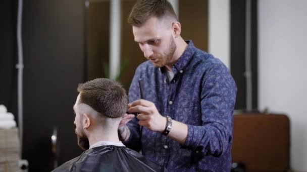 Frisör att göra snygg frisyr till oigenkännliga manlig klient sitter i stol i barbershop — Stockvideo