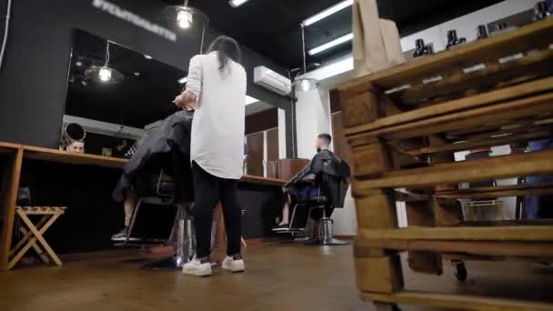 Visão traseira da mulher fazendo cabelo para clientes masculinos sentados na barbearia — Vídeo de Stock