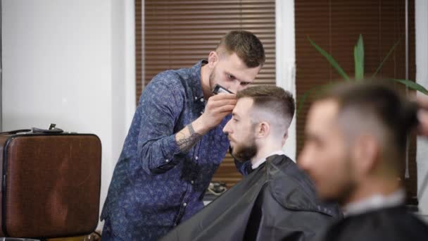 Barbiere concentrato utilizzando trimmer mentre rende elegante acconciatura al cliente in barbiere — Video Stock