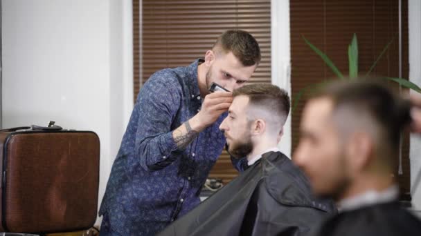 Peluquero concentrado usando trimmer mientras que hace el peinado elegante al cliente en la barbería — Vídeos de Stock