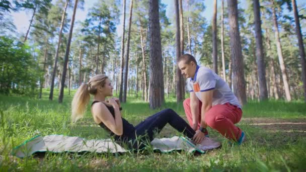 Veselá manžel a manželka dělá sportovní cvičení v parku na trávě, Žena je houpací lis, muž jí pomáhá tím, že drží její nohy — Stock video
