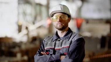 Üniformalı, çalışan insanın yakın koruyucu hardhat ve inşaat alanında ayakta ve kameraya bakarak gözlük. Gülümseyen ve başparmak yukarıya el hareketi inşaat alanında çalışan genç adam.