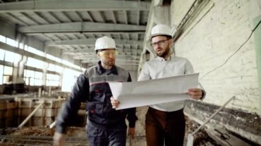 Gömlek ve pantolon alan bina boyunca işçi ile yürüme Denetçi giymiş. Profesyonel Müfettiş blueprint tutarak ve mufassal gelecekteki projesinin inşaat Başkomiser ile tartışıyor.