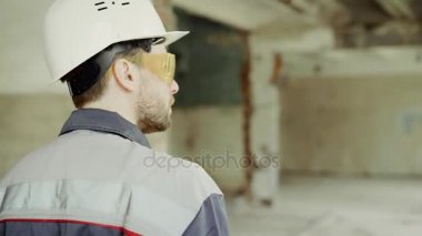 Arkadan görünüşü üniforma giymiş Müfettiş koruyucu hardhat ve inşaat alanında yürüyüş ve endüstriyel proje kontrol gözlük. Profesyonel surveyor inşaat alanı inceliyor.