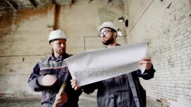 Profesyonel mühendisleri yeni proje üzerinde modern kentsel inşaat tartışırken planı ile şantiye yürüme. İnşaatçılar çalışma geliştirme soruşturma proje çizimleri ve teknik özellikleri.