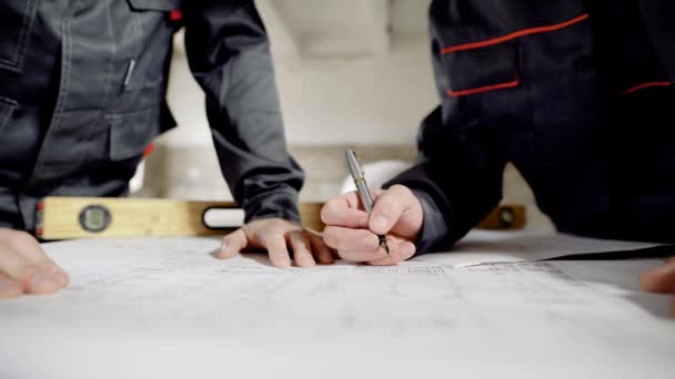 Close-up de mãos masculinas desenhando planos de design e especificação. Plano de construção e nível deitado sobre a mesa de madeira. Dois arquitetos trabalhando em canteiros de obras com documentação de desenvolvimento . — Vídeo de Stock