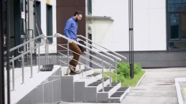 Genç yakışıklı sakallı adam mavi gömlek ve kahverengi pantolon dışarı gidiyor. Açık havada mutlu başarıyla yürüyen öğrenci sınavı geçti. Yeni iyi iş almak memnun yöneticisidir.