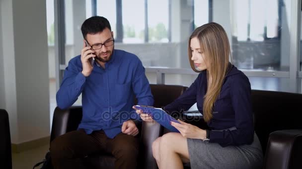 Les gens d'affaires travaillent ensemble dans l'immeuble de bureaux moderne avec des fenêtres en arrière-plan. L'homme parle au téléphone. Femme avec presse-papiers écoutant son collègue et prenant des notes . — Video