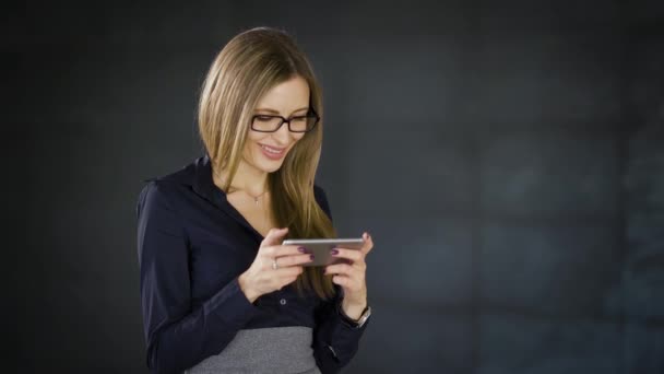 Primer plano de la mujer de negocios de pie en la oficina con la pared gris oscuro en el fondo escribiendo mensajes utilizando el teléfono inteligente. Mujer gerente de ventas charlando por medio de dispositivo digital durante la pausa del almuerzo . — Vídeos de Stock